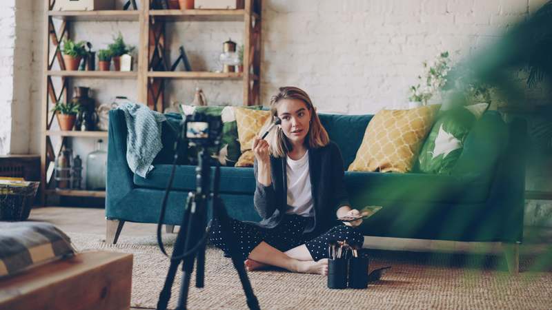Editorial photo of founder holding a makeup brush and vitamin bottle, surrounded by clean beauty products